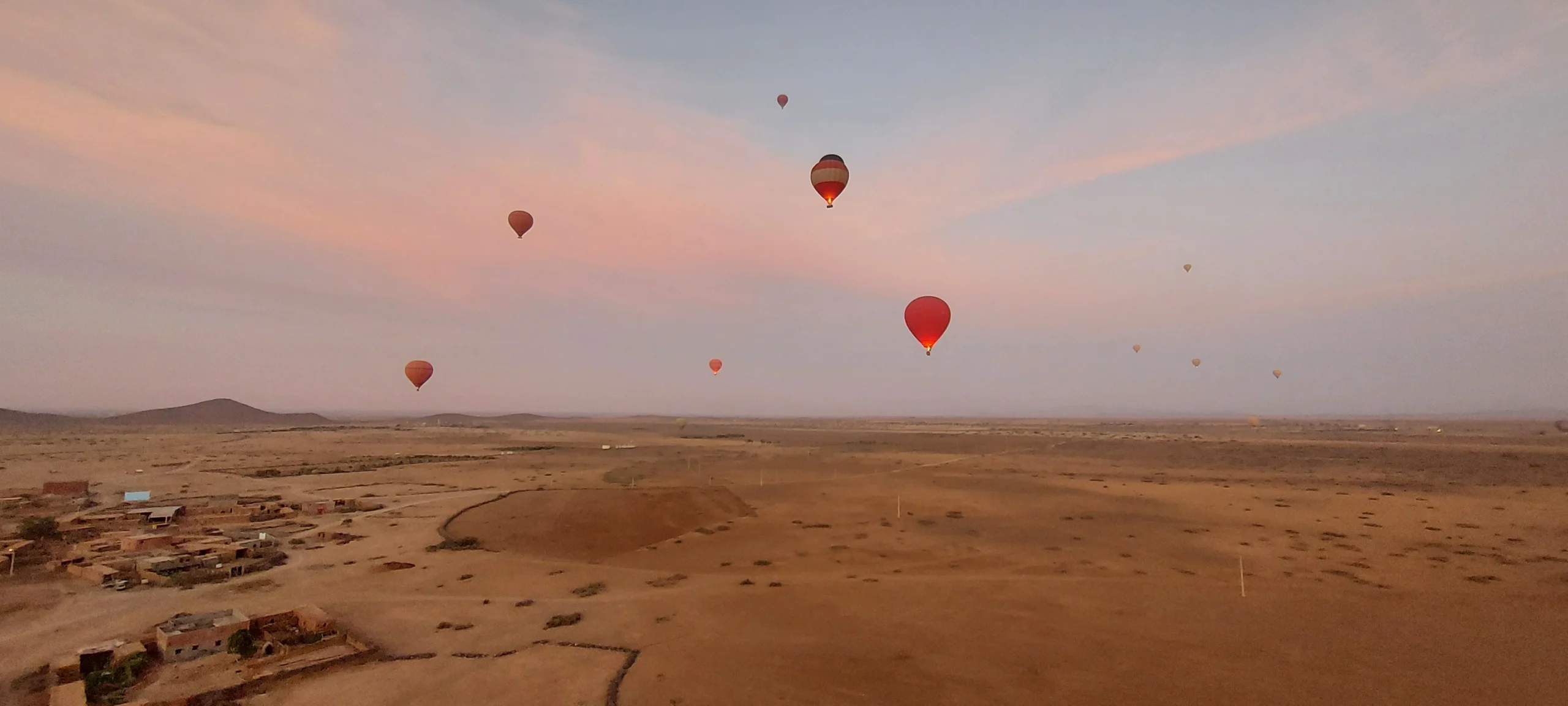 Sunrise hot air balloons drifting over the desert near Marrakech, Morocco, beneath a soft pink sky.