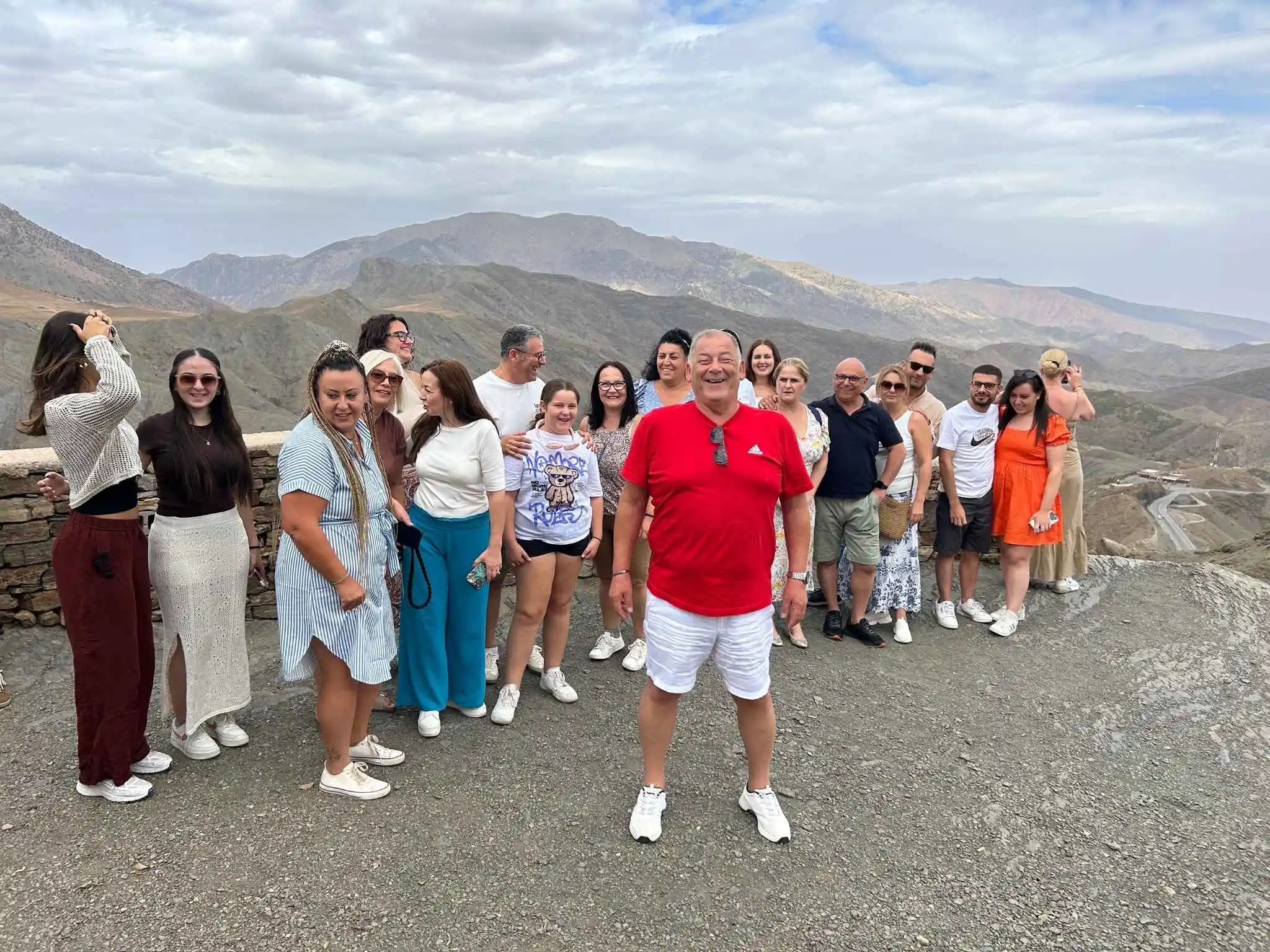 American travelers smiling with their Moroccan guide at a scenic Atlas Mountains viewpoint during a group tour.