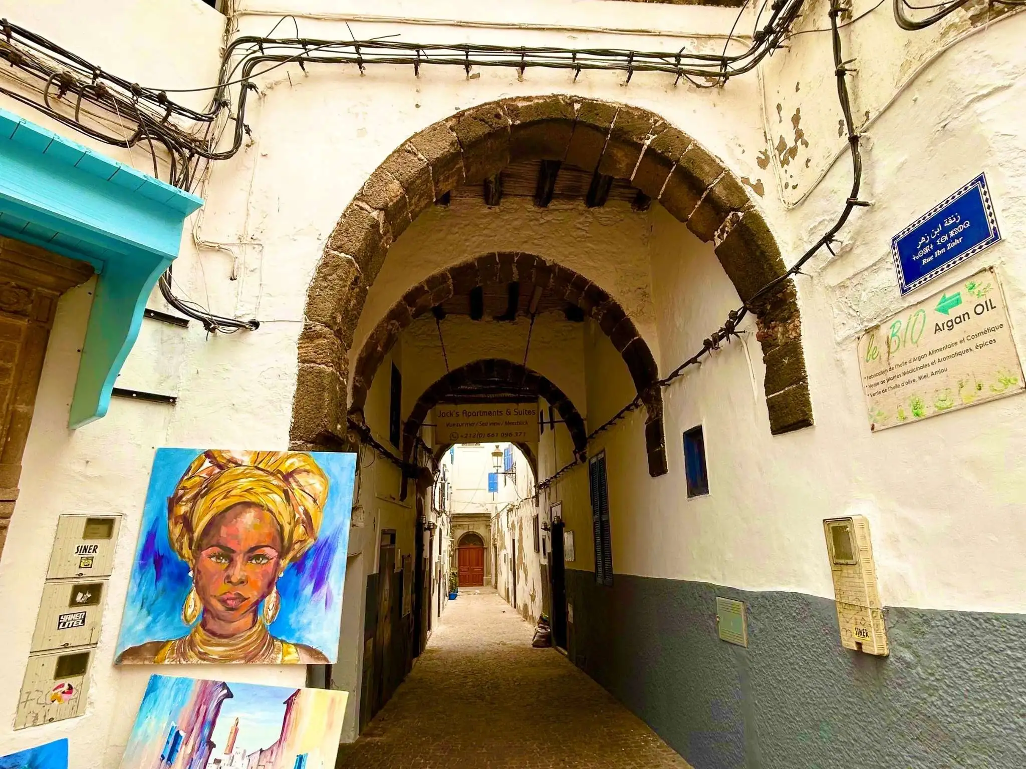 Narrow vaulted lane in Essaouira medina, Morocco, with colorful paintings and whitewashed walls under stone arches.