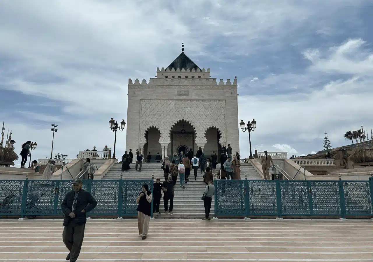 Visitors climbing the steps to the Mausoleum of Mohammed V in Rabat, framed by teal ironwork and lanterns.