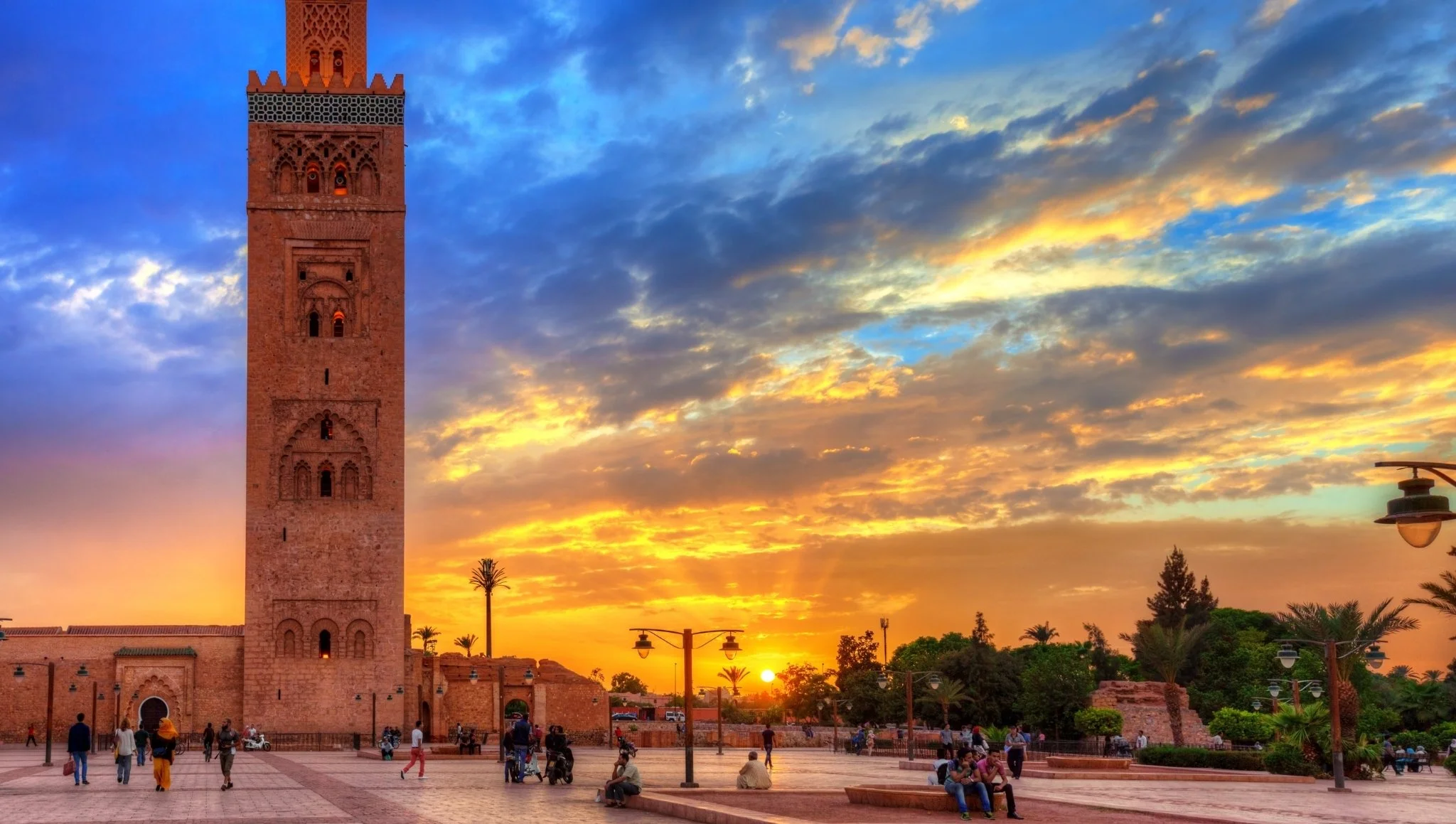 Wide view of the Koutoubia minaret glowing at sunset with people strolling across the open plaza in central Marrakech.