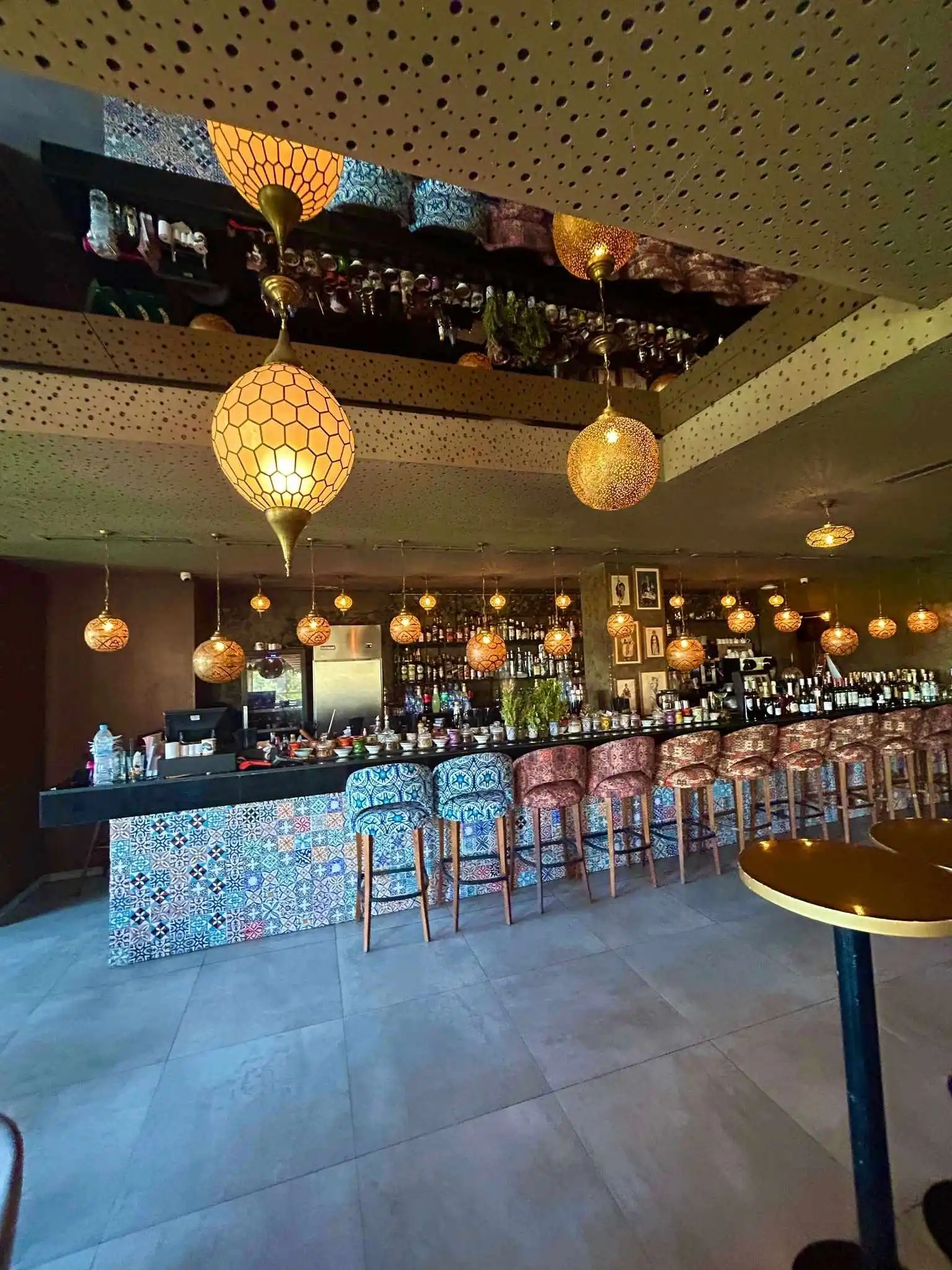 Warmly lit bar with hanging Moroccan lanterns and a mosaic-tiled counter.