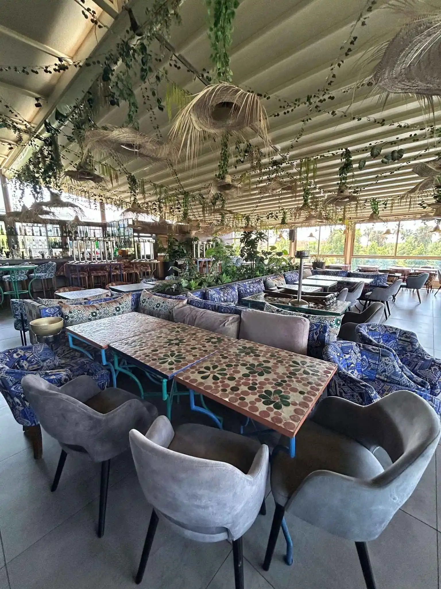 Spacious rooftop restaurant featuring mosaic tables, patterned sofas, and ceiling-hung plants.