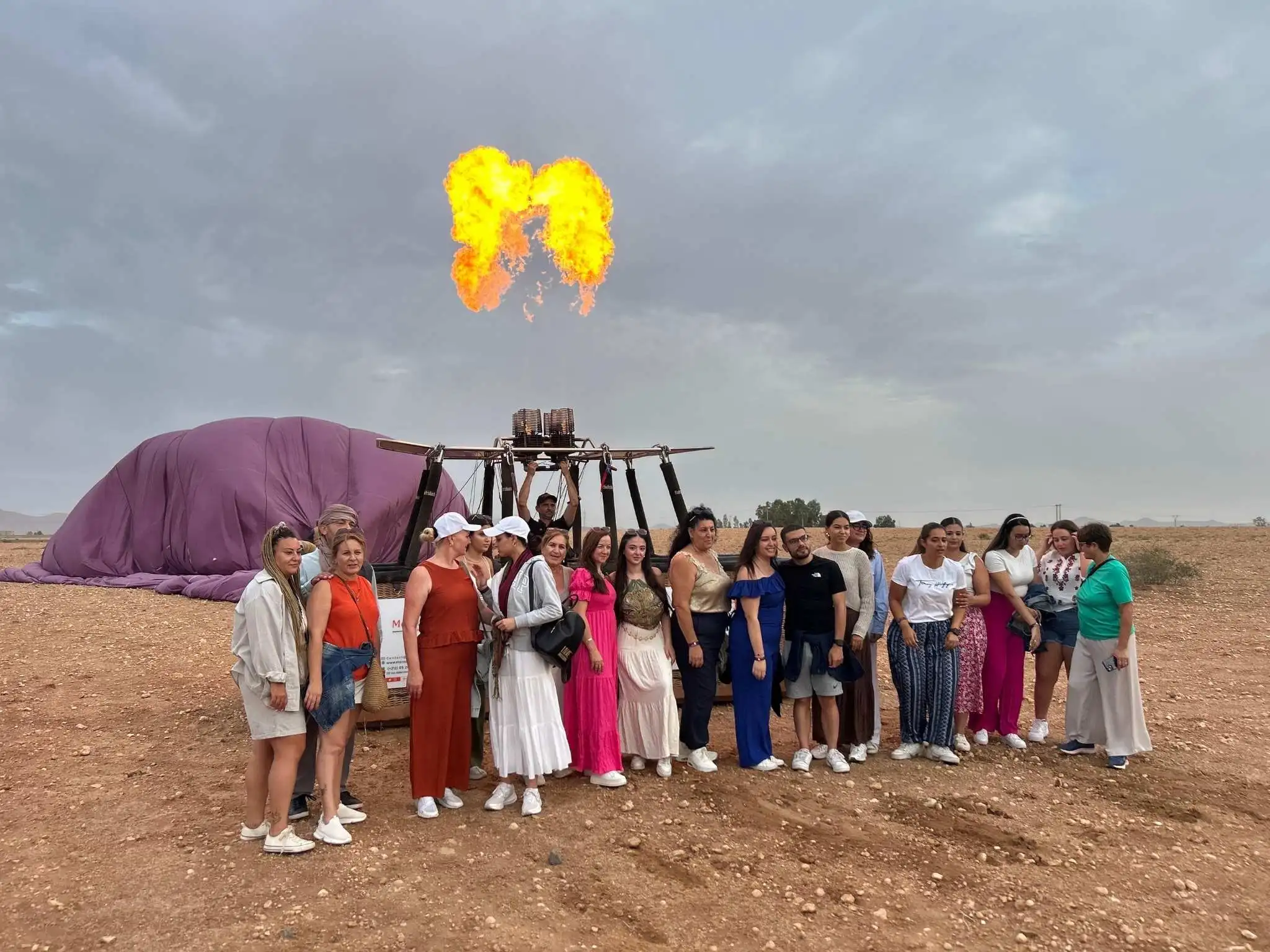 Mixed group of American visitors chatting with local crew beside a hot-air balloon burner near Marrakech.