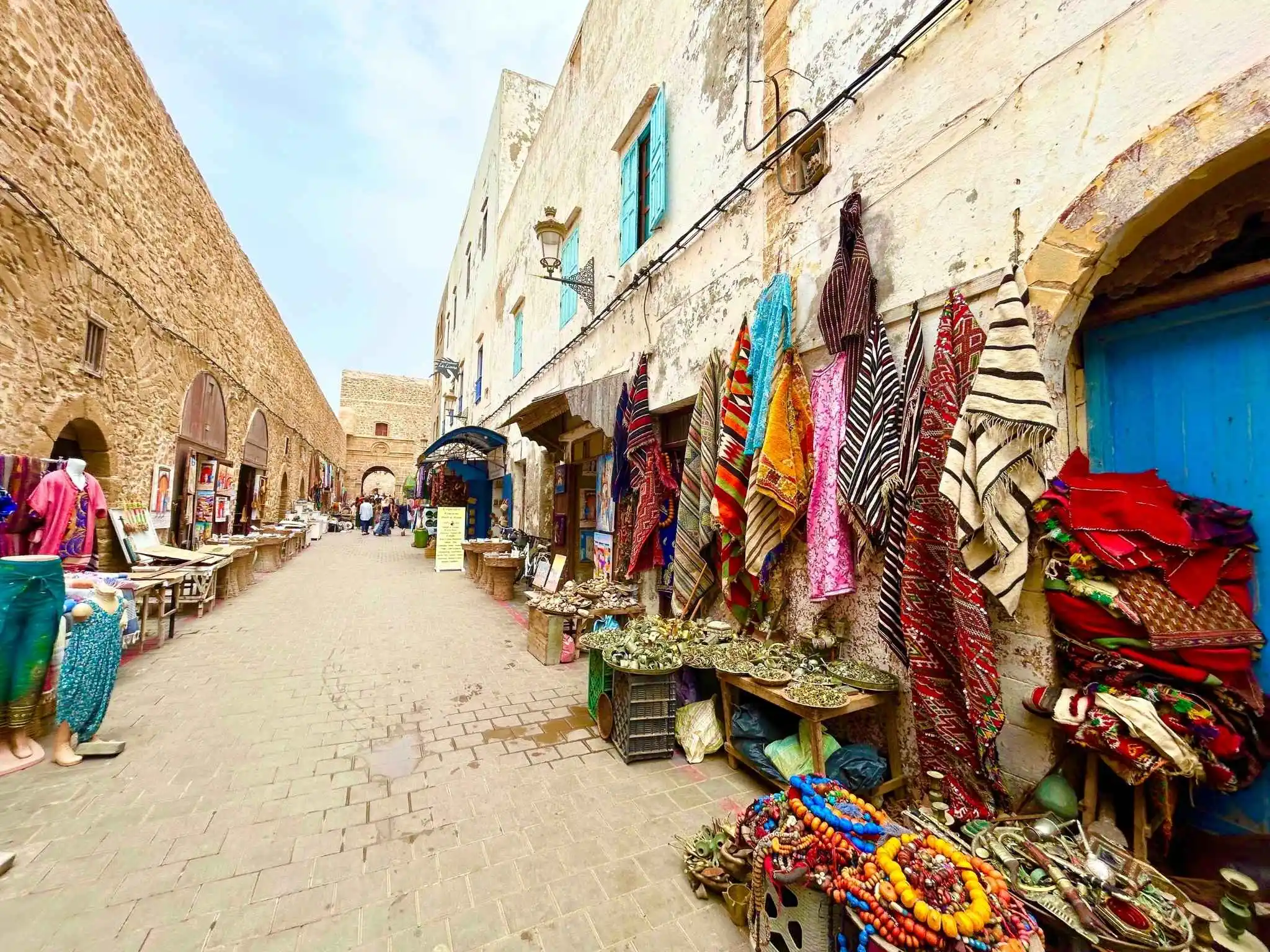 Lively souk street in Essaouira, Morocco with Berber rugs, jewelry and handicrafts displayed along stone alleys.