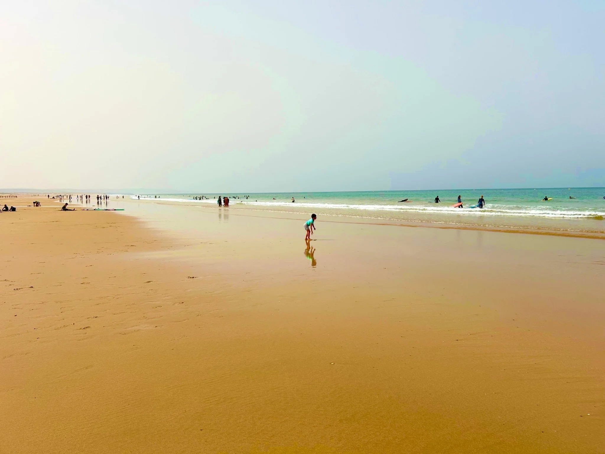 Families and surfers enjoying the long sandy beach and gentle Atlantic waves in Essaouira, Morocco.