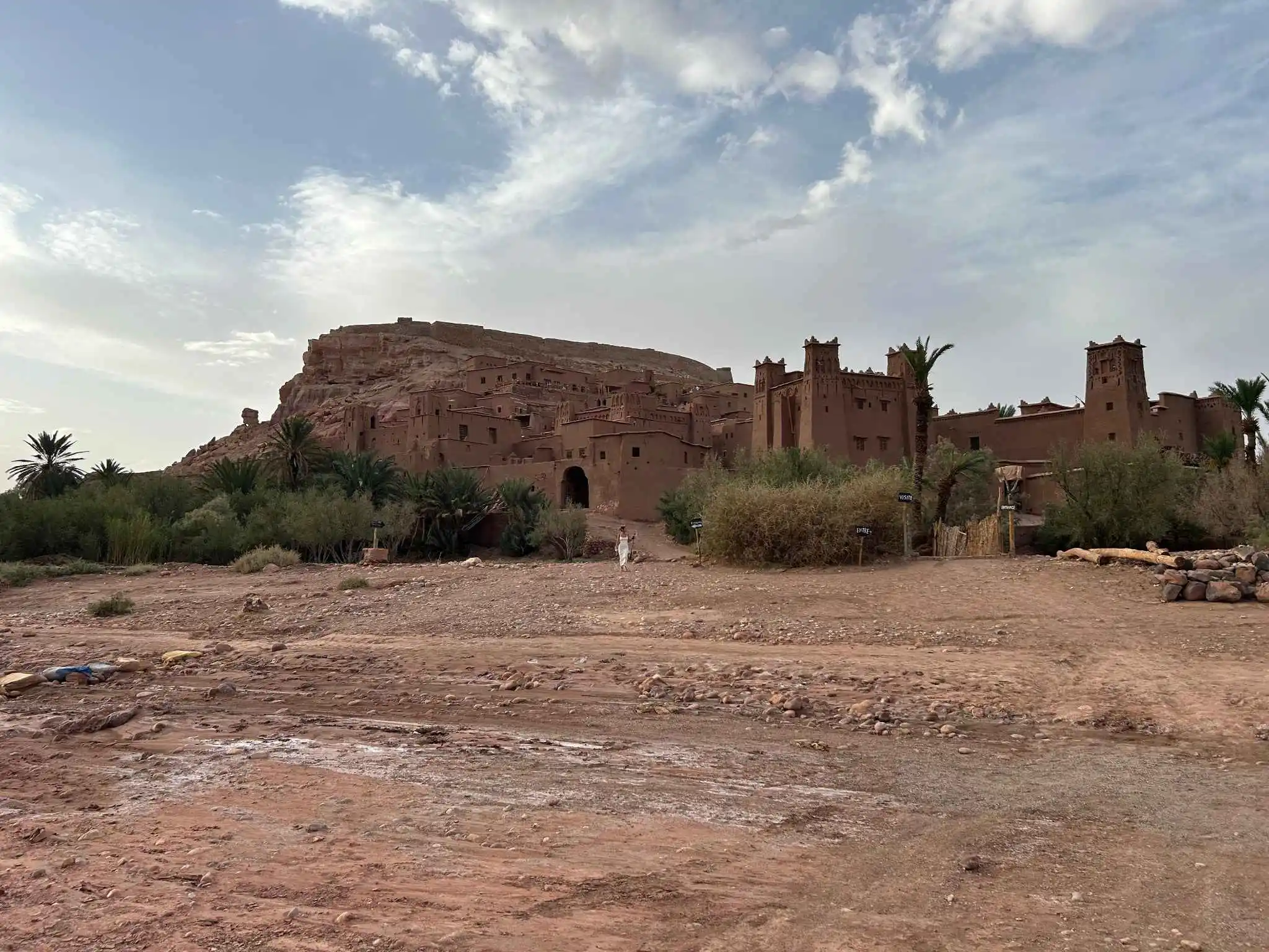 Aït Benhaddou ksar: Mud-brick towers climb a hillside beside palms under a soft, clouded sky. Marked trails and knowledgeable local guides help travelers tour the site safely while learning its caravan and film history.