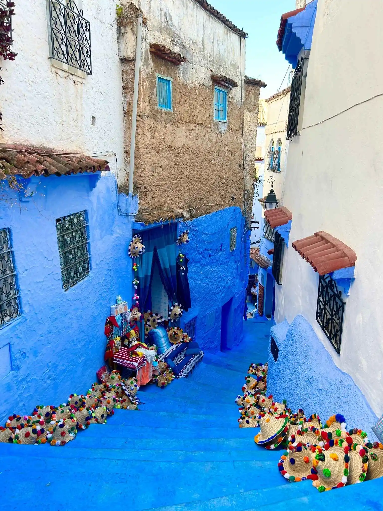 Chefchaouen blue stairs. Steep alley painted in vivid blues lined with pom-pom Berber hats and textiles cascading down the steps—and travelers can experience it with confidence in Morocco’s tourist-friendly environment.