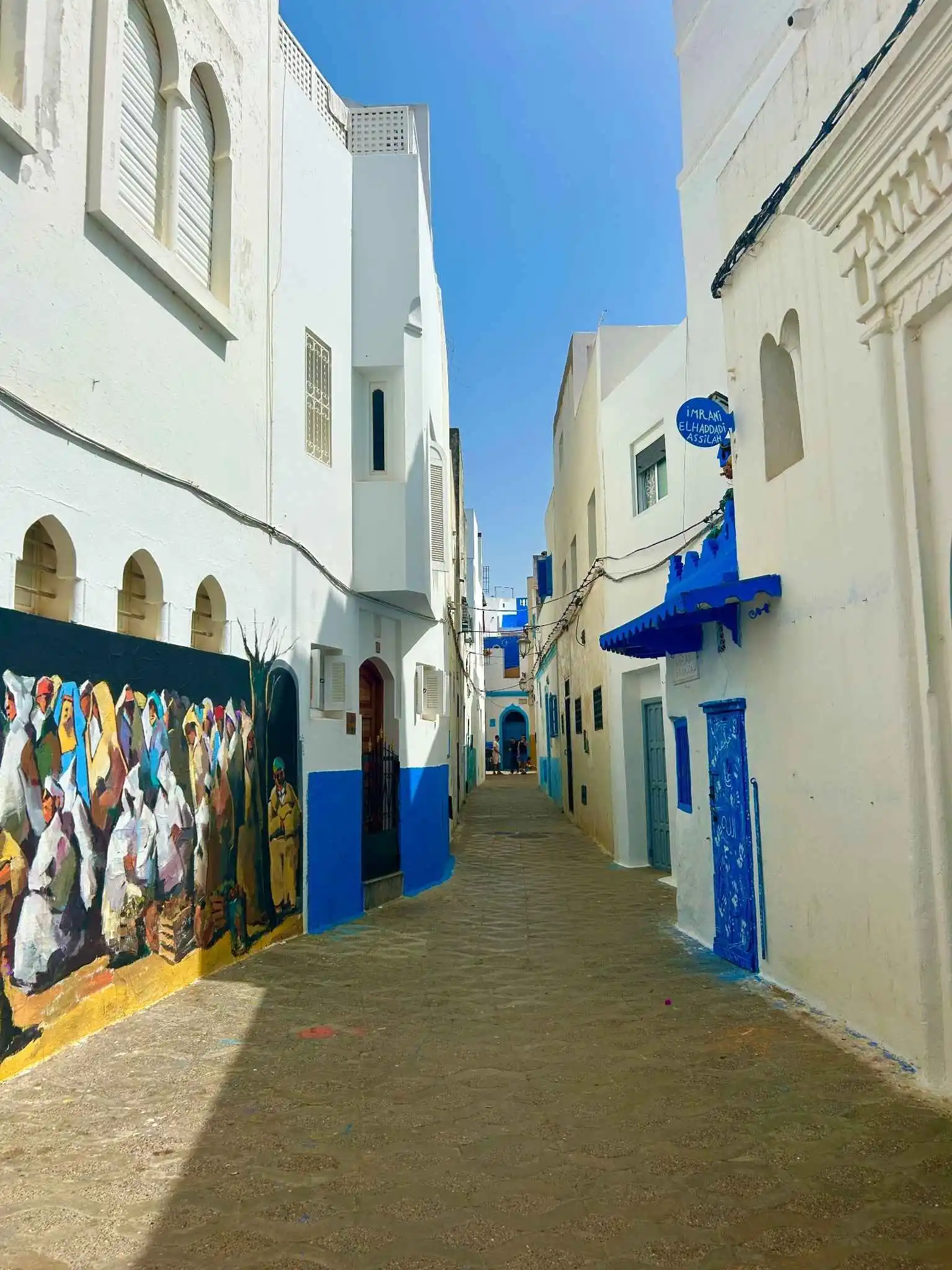Essaouira/Atlantic medina lane. Sun-washed white walls with blue trim and a lively mural line a narrow coastal alley—and enriching experience for visitors interested in Morocco’s coastal history. allowing travelers to discover the vibrant underwater life Morocco is famous for.