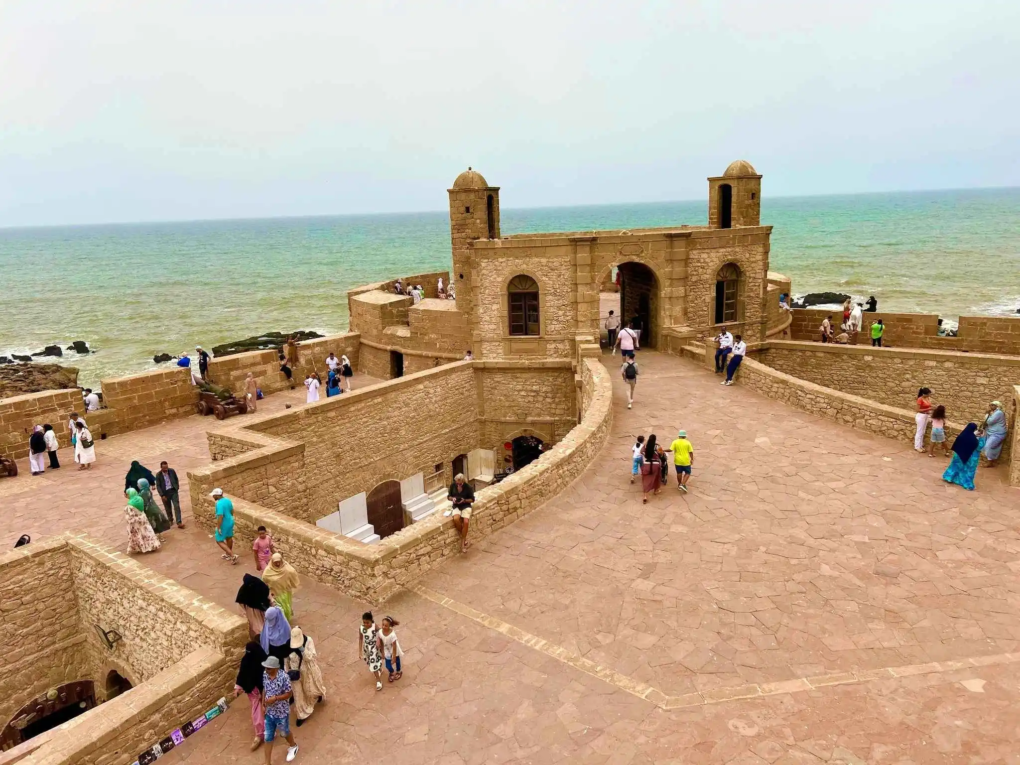 Skala de la Kasbah, Essaouira: Honey-stone ramparts and watchtowers overlook the ocean as people stroll the wide terrace. Well-kept walkways and visible staff create a calm, secure setting for sightseeing.