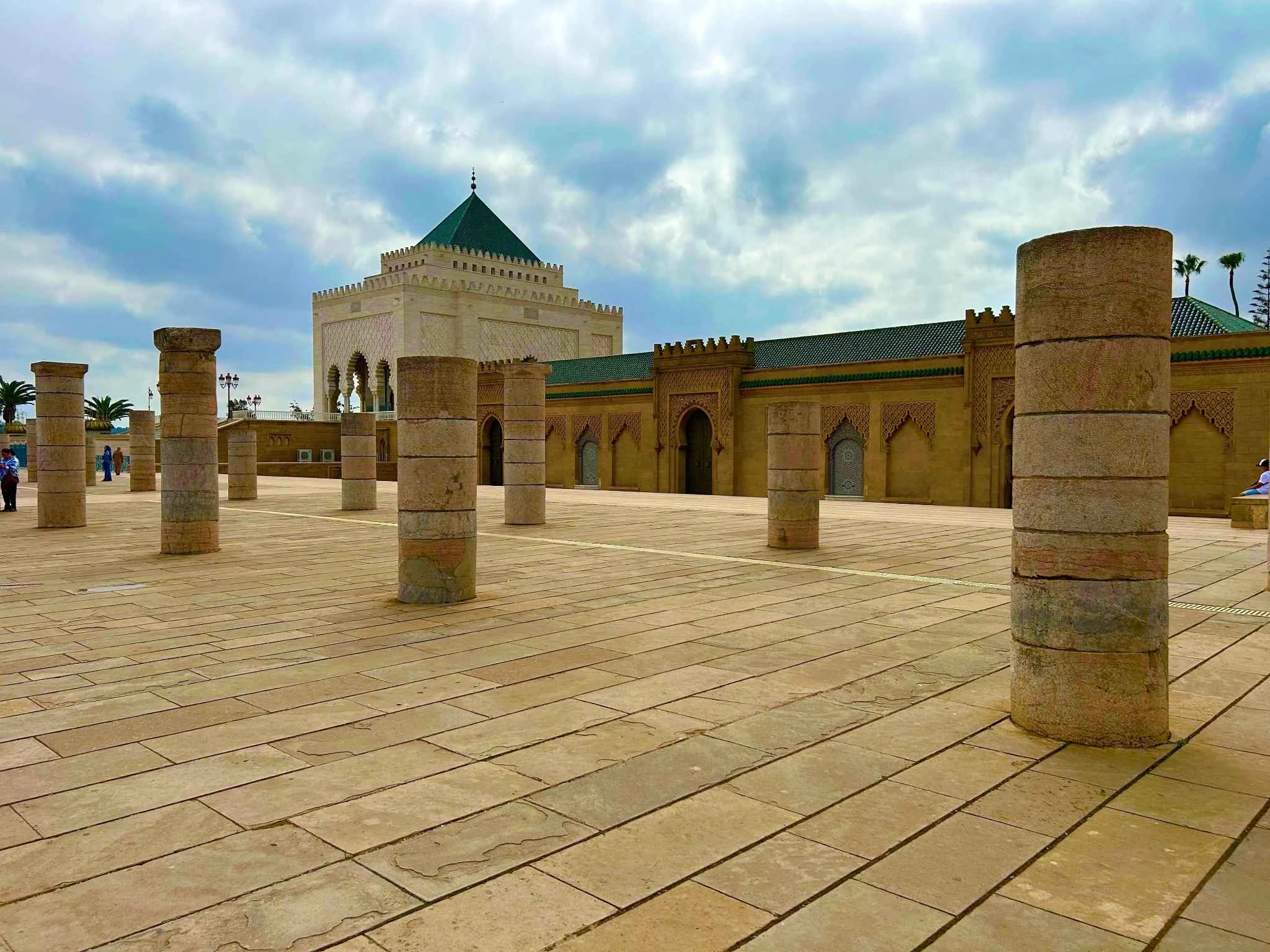Mausoleum of Mohammed V & Hassan Tower site (Rabat). Stone columns lead to the white mausoleum with green pyramid roof and carved arches—awe-inspiring destination for travelers interested in Morocco’s rich history.