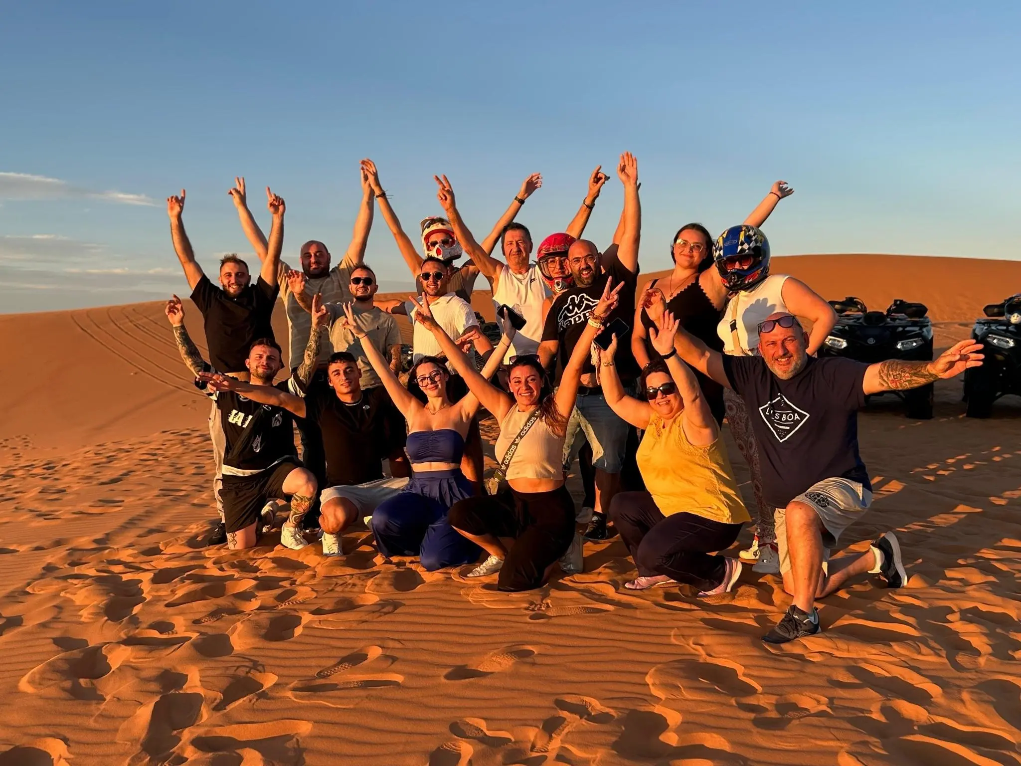 Group of travelers celebrating on Sahara sand dunes with quad bikes in the background on a 7-day Morocco desert and Chefchaouen itinerary.