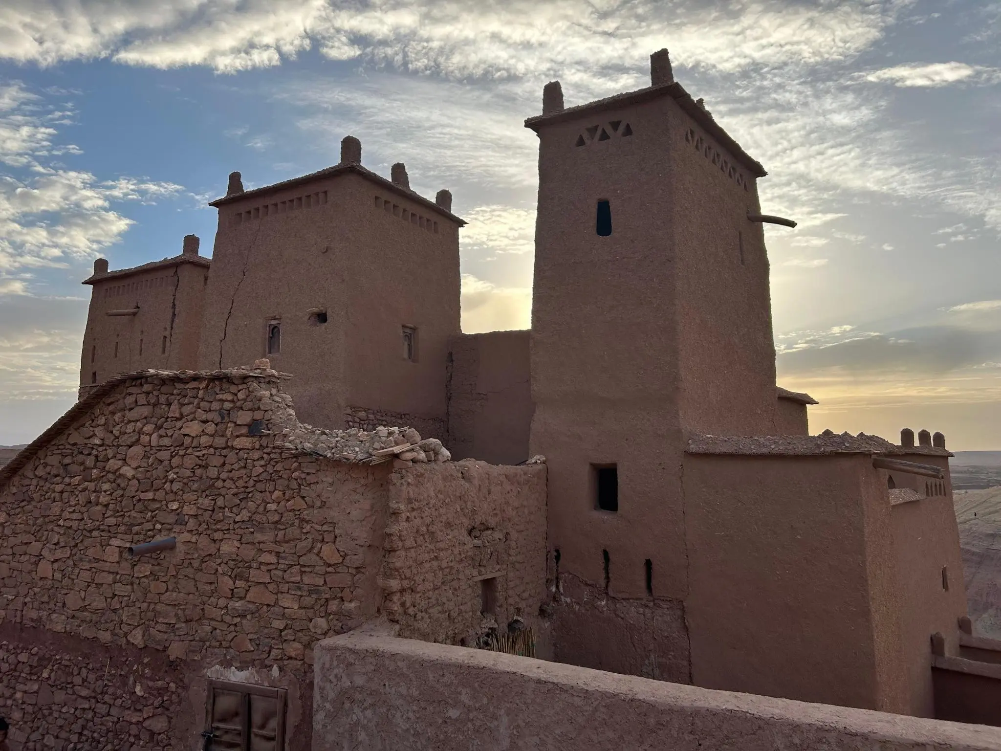 Earthen kasbah towers of Ait Benhaddou glowing at sunset with partly cloudy sky in southern Morocco.