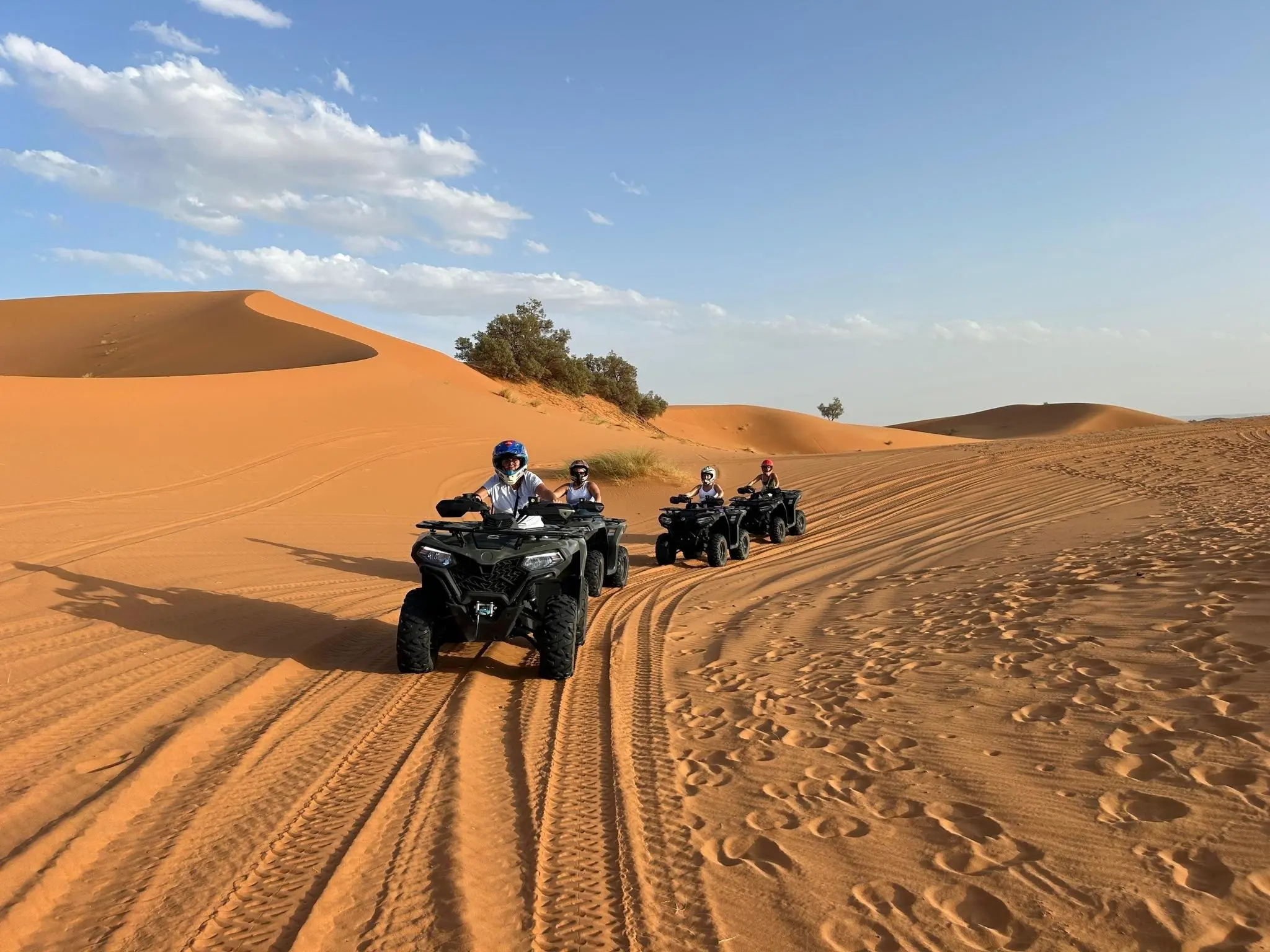 Riders on quad bikes tracing tracks across the orange sand dunes of Erg Chebbi near Merzouga, Morocco.
